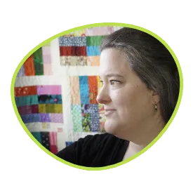 A woman looking to the left with a quilt behind her