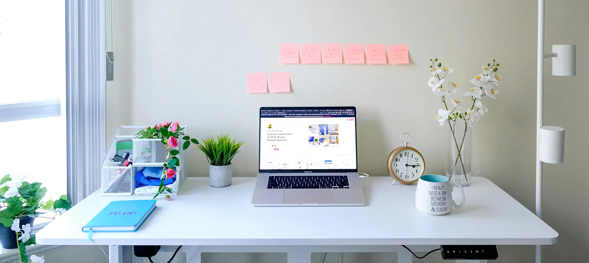 A workspace with a white desk with a laptop on it and post-it notes on the wall. Photo by Surja Sen Das Raj on Unsplash.
