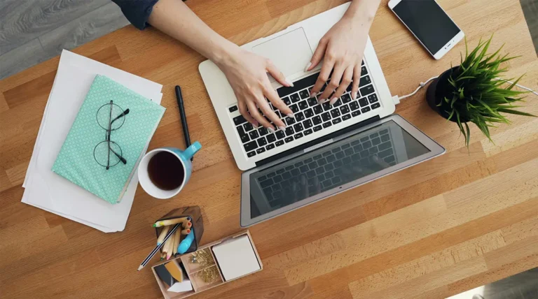 A overhead shot of a desk with a person's hands on a laptop keyboard