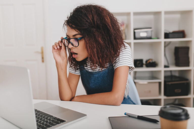 Young woman in striped shirt looking at laptop screen and holding glasses. Image by lookstudio on Freepik